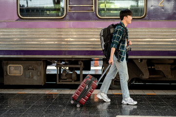 An Asian man with a backpack and a luggage catching the train at a railway station. side view image