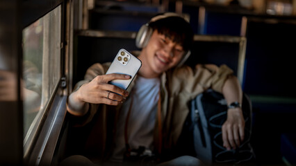 A happy Asian man is taking selfies with his smartphone while he is on a train somewhere in Asia.