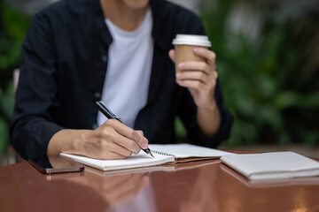 A man writing something in his book and sipping coffee at a table in a coffee shop.