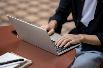 Close-up image of a man using his laptop computer, sitting at a table outdoors, working remotely.