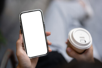 Close-up image of a man holding a white-screen smartphone and a coffee cup while sitting outdoors.