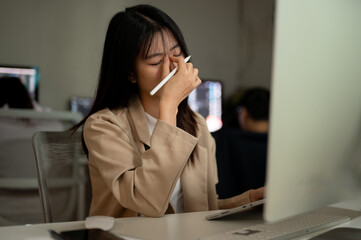 A tired and overworked Asian businesswoman is working on her project on computer in the office.