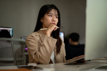 Young concentrated Asian businesswoman is working in the office, looking at her computer screen.