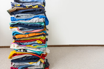 A very tall stack of folded colored clothes for charity, washing, ironing and sorting.