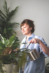 A young woman enjoys caring for flowers. Watering indoor plants and admiring them. 