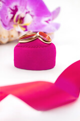 Gold wedding rings on pink velvet gift box with orchids on white background. Marriage, proposal, Valentine's Day. Vertical. Copy space