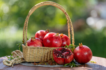Red Pomegranate in wooden basket on wooden table in garden, Pomegranate with slices on blurred greenery background.