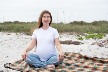 Caucasian pregnant woman meditating at the beach. Happy pregnant woman connecting with nature. 