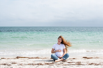 Fototapeta na wymiar Happy pregnant Caucasian woman with long hair meditating near the ocean 