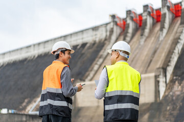 Confident asian two maintenance engineers man inspection discussstion with tablet at construction site dam with hydroelectric power plant and irrigation. Team engineer man working at project