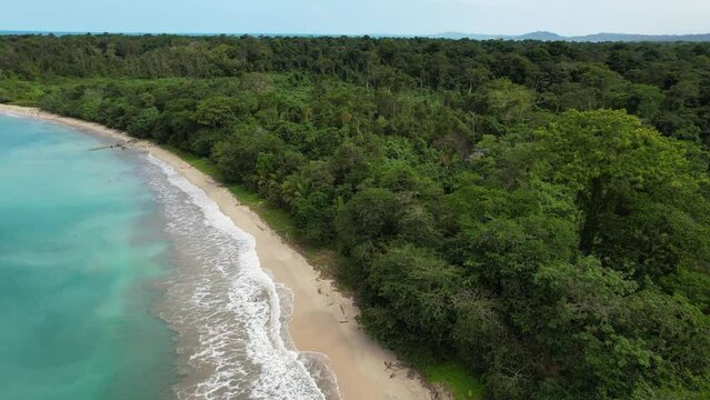Flight over a paradisiacal beach with turquoise water bordered by a jungle.