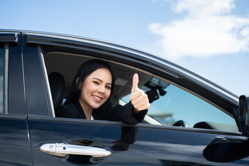 Young beautiful asian business women in suit getting new car showing thumbs up. She very happy and excited. Smiling female driving vehicle on the road on a bright day.