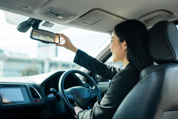Young beautiful asian business women in suit getting new car adjust rear mirror of car for driving safety. She very happy and excited. Smiling female driving vehicle on the road on a bright day. - Powered by Adobe