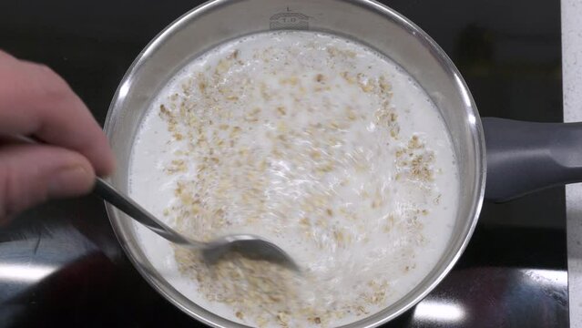 cooking oat flakes in boiling milk in a pan, cooking oatmeal porridge in saucepan on the stove