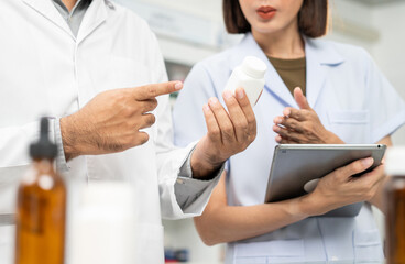 Obraz premium Two asian man and woman professional Pharmacist colleagues working at drugstore pharmacy. Asking the questions of medication standing near pharmacy shelves counter with medicines