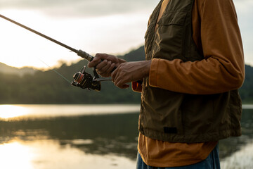 Enjoy moment of Handsome man fishing as a leisure activity during his vacation at the lake on sunset. Silhouette at sunset moment of man fishing rotation with reel.