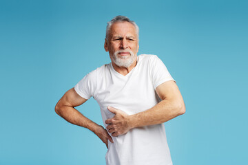 Portrait of upset gray haired elderly man holding back has pain, injury, problem, looking away