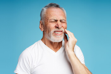 Upset mature retired man wearing white casual t shirt with toothache isolated on blue background - Powered by Adobe