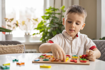 A Caucasian light-haired boy of five years old with blue eyes is putting together a puzzle 