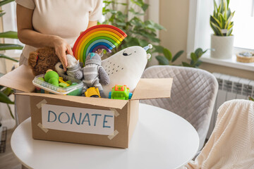 A woman puts toys in a cardboard box for charity. Donation concept.