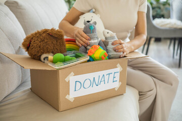 A woman puts toys in a cardboard box for charity. Donation concept.