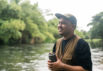 Young asian man traveller relaxing drinking coffee in nature forest and river background. Happy...