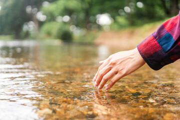 Close up woman hand touching water at river in mountains campsite nature background. Female Hand touching fresh water for refreshment. Human life and nature