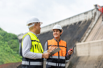 Confident asian two maintenance engineers man inspection discussstion with tablet at construction site dam with hydroelectric power plant and irrigation. Team engineer man working at project