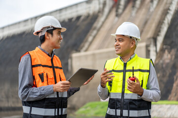 Confident asian two maintenance engineers man inspection discussstion with tablet at construction site dam with hydroelectric power plant and irrigation. Team engineer man working at project