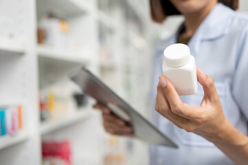 Close up woman hands holding medicine bottle near drug shelves. Pharmacist checks inventory of...