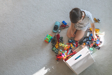 A cheerful European boy plays with cars on the carpet in his room. 