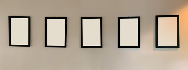 Five blank picture frames with black border hanging on the wall with copy space for text