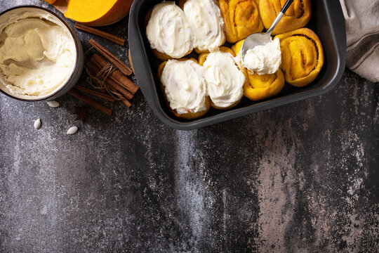 Freshly baked pumpkin cinnamon rolls or cinnabon with cream cheese on a dark stone background. Homemade seasonal autumn homemade pastry. View from above. Copy space.