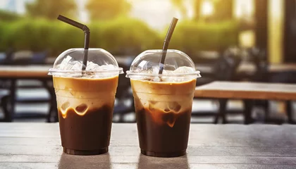Poster Plastic takeaway cups of delicious iced coffee on table in outdoor cafe with blurry background © Loliruri