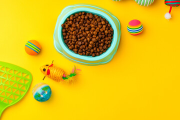 Cat bowl with dry food and toys on yellow background studio shot