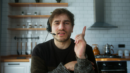 Man sitting in kitchen at home wears wireless headset with microphone talking to camera making...