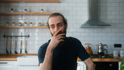 A bearded man sitting in modern kitchen at home talking to camera making conference business call....