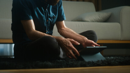 A man with sitting on the floor at home using an app on a tablet computer, playing games, having a...