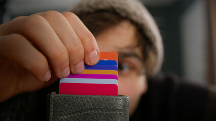 Close-up of young man in beanie opens card wallet full of credit cards looks at it 