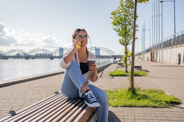 Young happy woman talk on phone and sitting in city street, drinking coffee in between work. Freelancer. Portrait of hipster female talking about new project. 