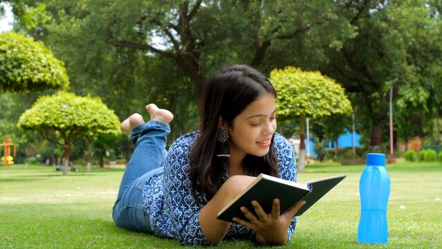 A pretty Indian girl relaxing and reading book - enjoying the sunny weather. Young girl spending leisure time in the park while reading a novel  - de-stress activity  bibliophile  calm nature  mind...