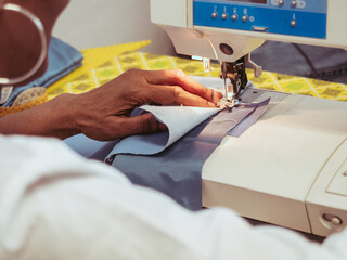 close up of adult black seamstress desginer hands use sewing machine to sew a shirt with precision...