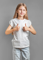 Happy child, little girl showing thumbs up gesture in a white T-shirt