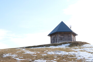 晴れた冬の終わりに青空の下雪解けの丘にたたずむ古い小屋
