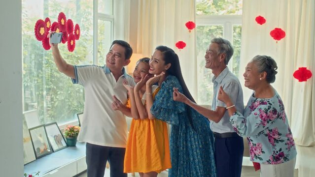 Long shot of big Vietnamese multi-generational family gathering in living room and taking selfie on smartphone during Tet celebrationLong shot of big Vietnamese multi-generational family gathering in 