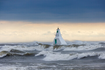 the sea waves crash in front of the light house as the sun sets