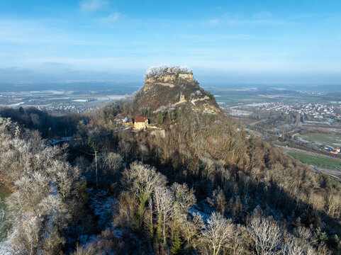 Luftbild vom verschneiten Hegauvulkan Hohenkr&auml;hen, mit Mauerresten einer Burg, umgeben von frostigen B&auml;umen in einer Winterlandschaft.