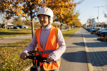 Portrait of a happy woman in vest and helmet driving an electric scooter on a street.