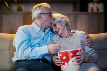 A romantic senior couple is kissing and relaxing with movie at home.