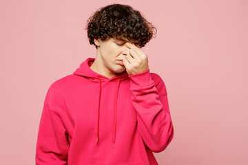 Young dissatisfied displeased sad Caucasian man he wears hoody casual clothes : keep eyes closed rub put hand on nose isolated on plain pastel light pink background studio portrait. Lifestyle concept.